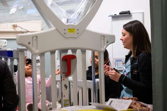 Karleen Wray speaking to two year old, Genesis, who is sitting in a crib