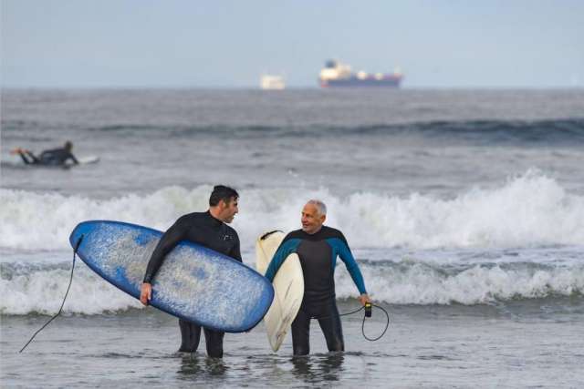 Dr. Sassoon and Robert Lombard walking with their surfboards on the beach while talking