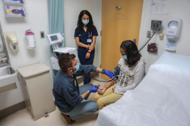 Doctor checking a female patient's blood pressure. A nurse standing by their side.