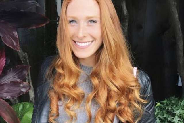 A portrait of Sarah Adler, a smiling woman with long red hair and a black leather jacket.