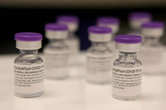Several Pfizer-BioNTech COVID-19 vaccine vials with purple caps arranged on a table.