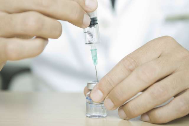 A healthcare professional preparing a syringe from a vaccine vial.