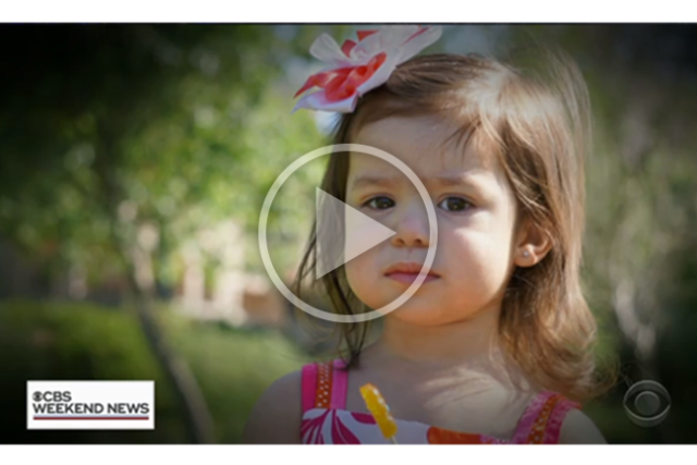 CBS news video thumbnail of a little girl with a flower in her head standing in a park.