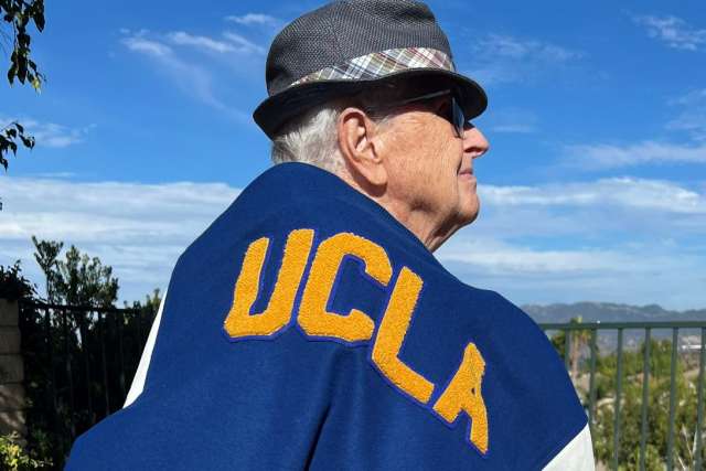 A man wearing a fedora has a UCLA jacket over his right should.