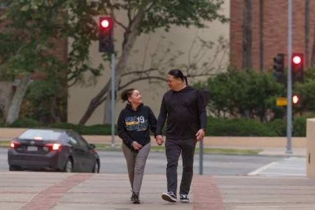 Two people walking hand in hand on a brick pathway near a street intersection with a red traffic light and a parked car.