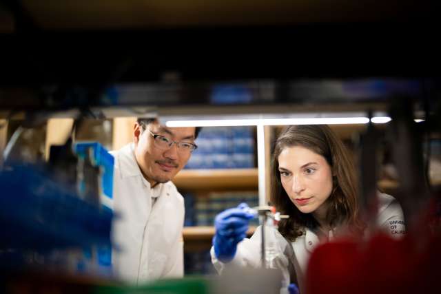 Two scientists in a lab examining a sample, one holding a pipette.