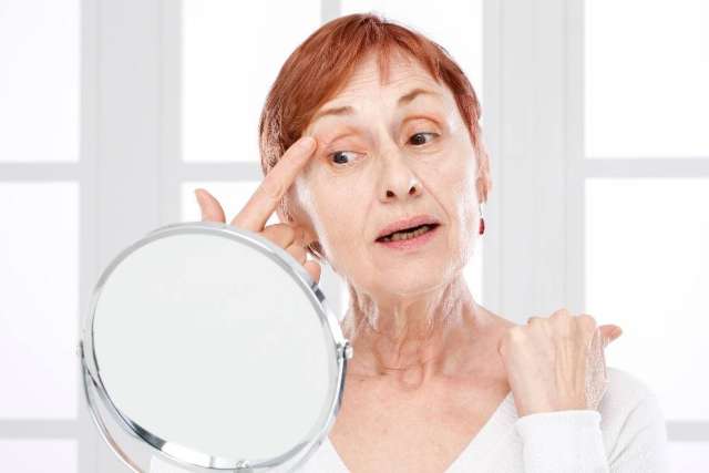 Older woman checking her face in a handheld mirror