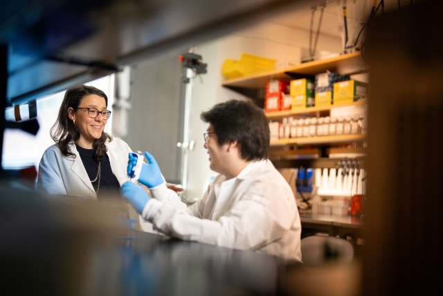 Two researchers in lab coats collaborate while one uses a pipette