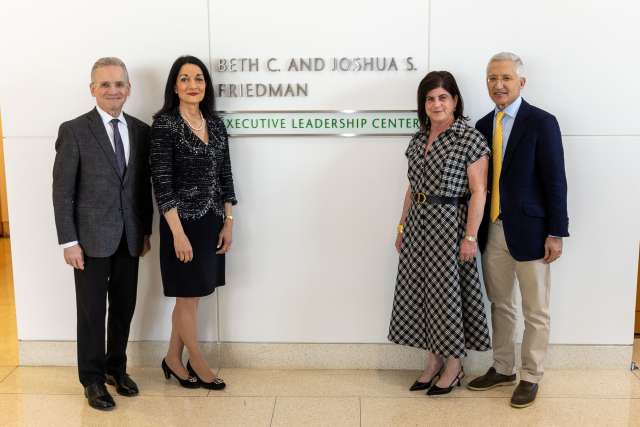 Four people pose together in front of a sign for the Friedman Executive Leadership Center.
