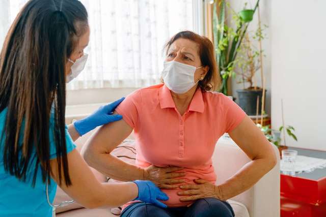 A healthcare professional assists a woman experiencing abdominal pain at home.