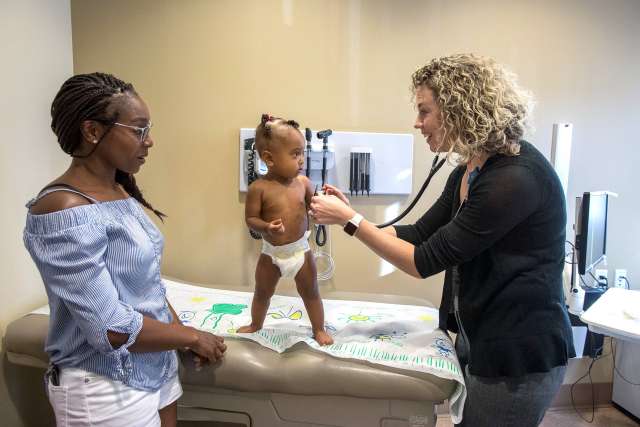 Allison E. Guimera MD examining a toddler on an exam table while the mother watches