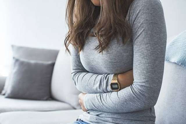 Woman clutching lower abdomen on couch