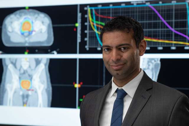 Dr. Amar U. Kishan standing in front of four monitors displaying body scans