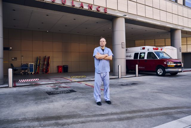 A doctor in scrubs stands in front of the ER.