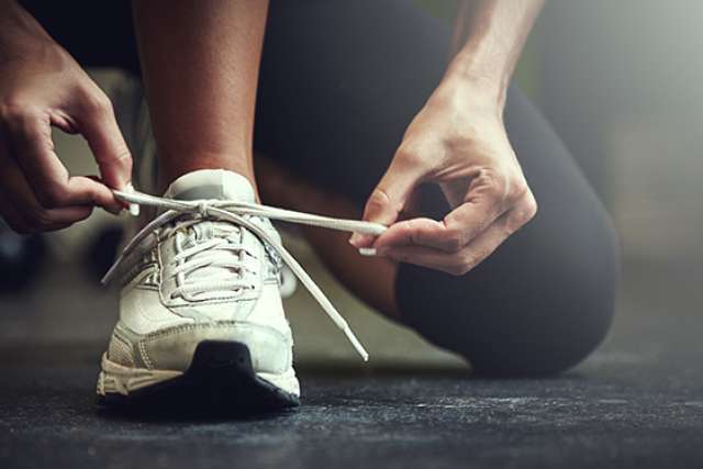 A close-up of a person tying the white laces of a white running shoe while wearing black athletic pants.