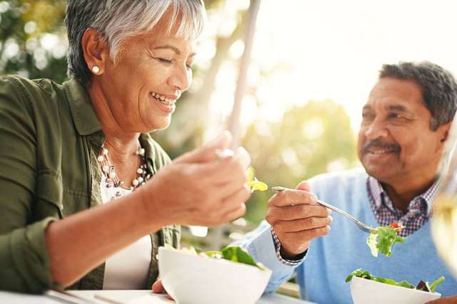 Two people smiling while eating salad outdoors