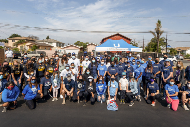 Large group of masked UCLA Health volunteers and community members pose together outdoors under a branded canopy tent.