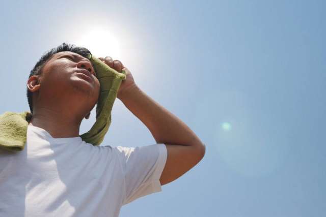 Man outside in hot sun wiping his brow