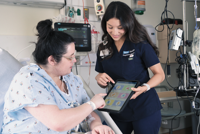 Nurse assisting a patient with a tablet in a hospital room.