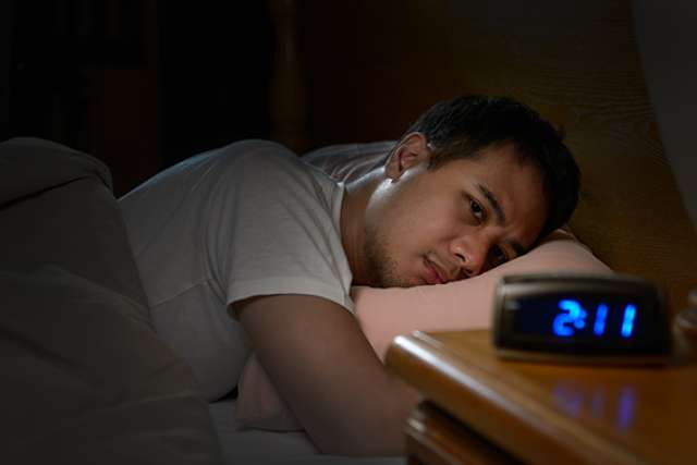 Man awake in bed staring at alarm clock reading 2:11