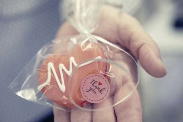 A close up image of someone holding a heart shaped cookie with heartbeat-rhythm shaped icing. The cookie is wrapped in a plastic bag with a ribbon and a pink sticker that says "thank you" with a heart