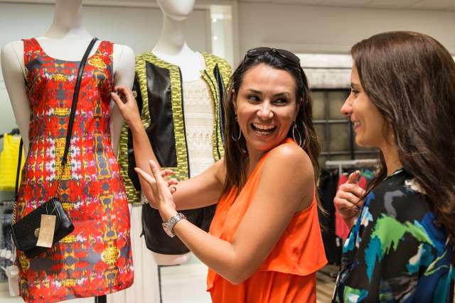 Three women in a boutique; smiling woman shows a bracelet to a friend.