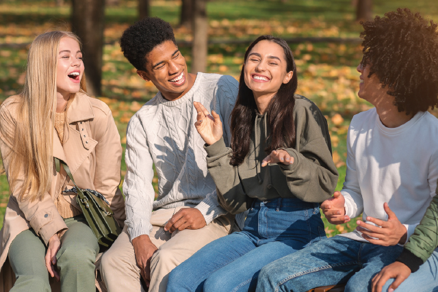 Four friends laughing on a park bench in autumn