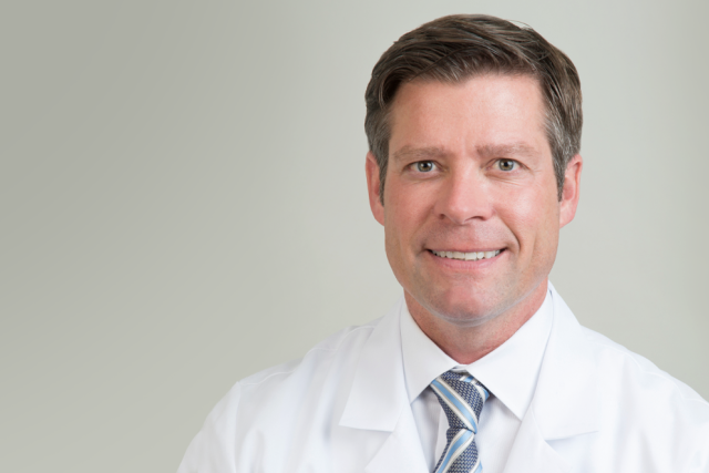 Jesse Mills, MD smiling and wearing his lab coat and a striped tie.