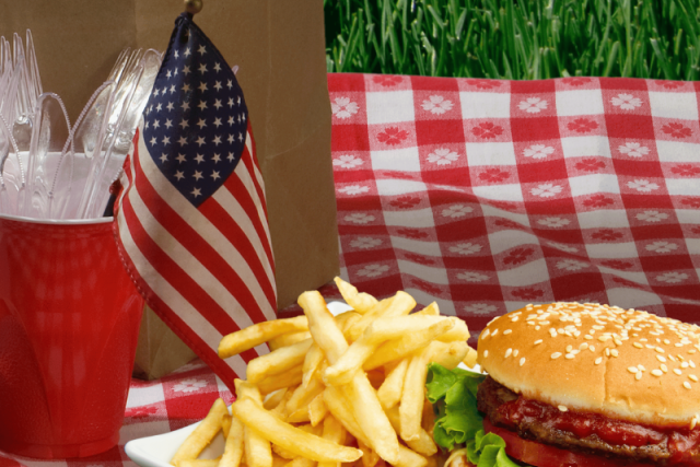 Burger and fries on red-checkered picnic cloth with small American flag