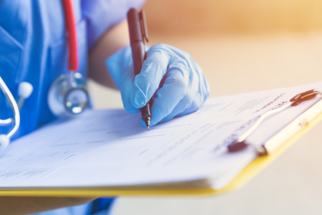 Medical professional filling out a patient form on a clipboard.