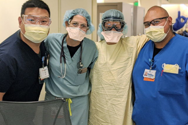 UCLA Health care team members wearing scrubs, PPE, and face masks pose together in a hospital unit during the COVID-19 pandemic.
