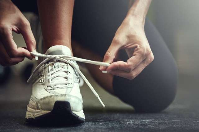A person tying the laces of a white athletic shoe.