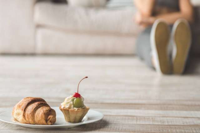 Croissant and cherry-topped cupcake on plate, blurred person on sofa
