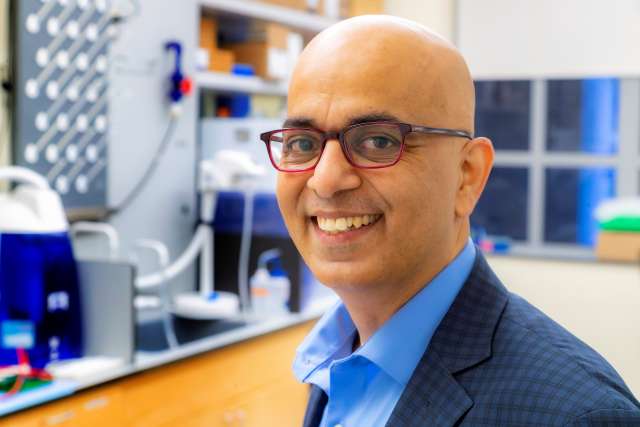 Smiling man with glasses and suit standing in a laboratory