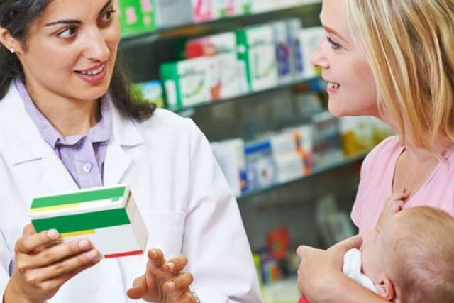 A pharmacist discusses medication with a mother holding a baby in a pharmacy.