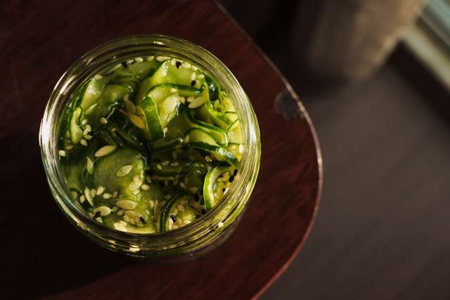 Jar of sliced cucumbers in vinegar on a wooden surface.