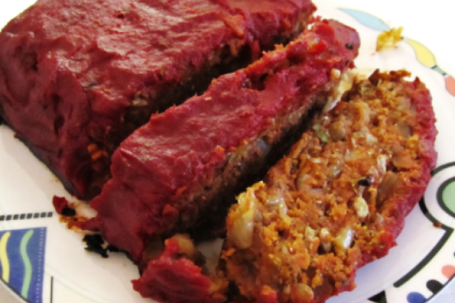 Sliced lentil loaf topped with tomato glaze, served on a white plate with visible grains, vegetables, and legumes.