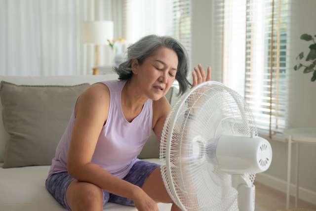 Woman sitting at home cooling herself with a floor fan
