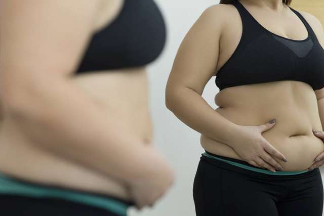 Woman in sports bra examining her stomach in a mirror
