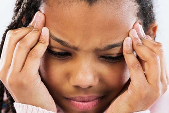 Close-up of two hands holding braided hair strands near the head. The person is wearing a light-colored long-sleeve top, and the background is softly lit.