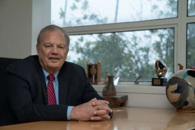 Dennis Slamon, MD, PhD sitting at his desk wearing a suit and tie