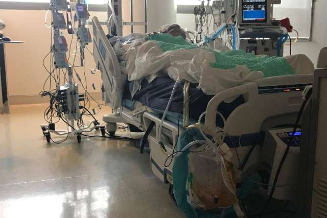Hospital patient lying in a bed connected to multiple monitors and medical equipment in an intensive care setting.