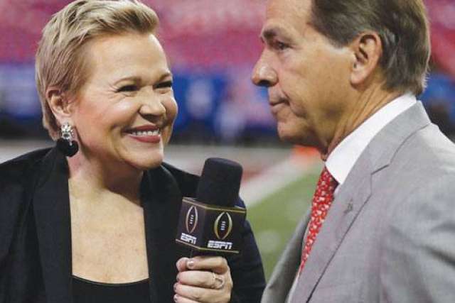 A woman interviews a man in a suit on a sports field.