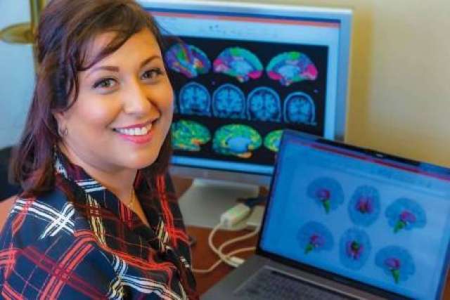 Arpana Gupta sitting at a desk with brain scan images on two screens.