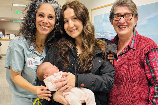 A new mom holds her baby, with her doctor and her own mother by her side.