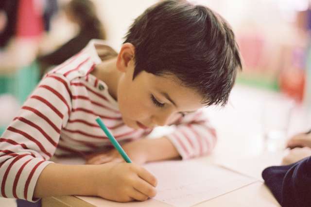 A young child concentrates while writing at their desk.