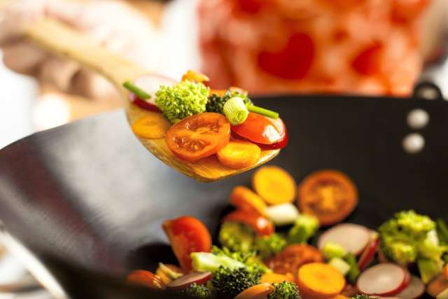 Colorful vegetables being stirred in a black wok.