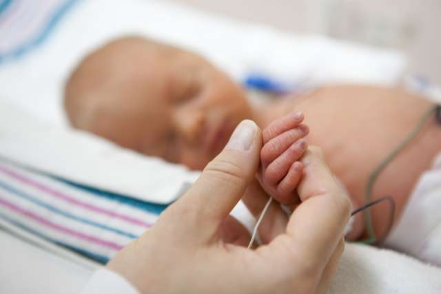 Baby in the NICU holding on to mom's hand.