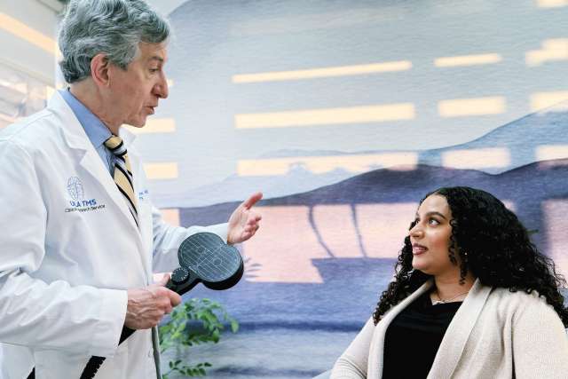 UCLA Health Dr. Andrew Leuchter speaks to a patient while holding a transcranial magnetic stimulation coil.