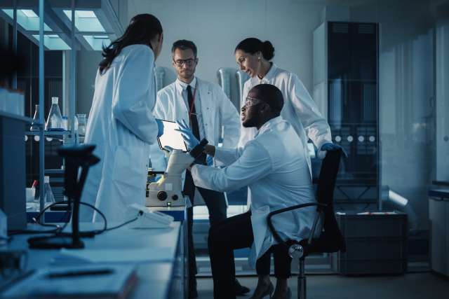 Group of researchers huddle together and collaborating in a lab